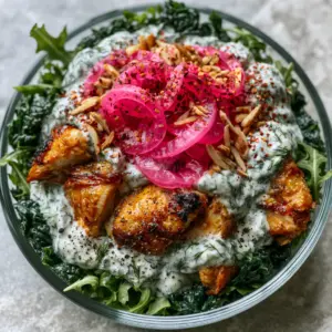 Close-up of hand-torn roasted chicken salad with glistening skin, emerald kale, and thick white herb dressing sprinkled with black pepper.