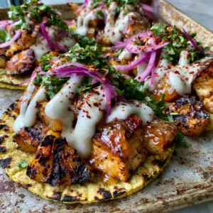 Close up overhead shot of vibrant pineapple chicken tacos with purple onions and bright green cilantro garnishes.