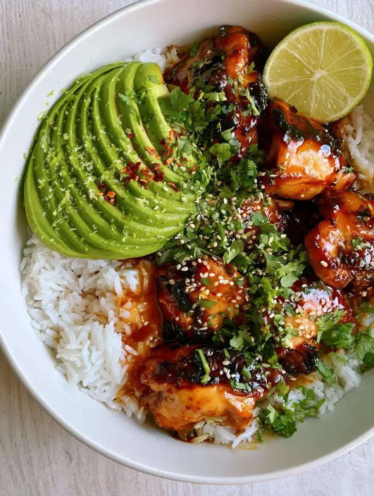 Overhead view of a white ceramic bowl filled with jasmine rice, honey lime chicken, and fan-sliced green avocado.