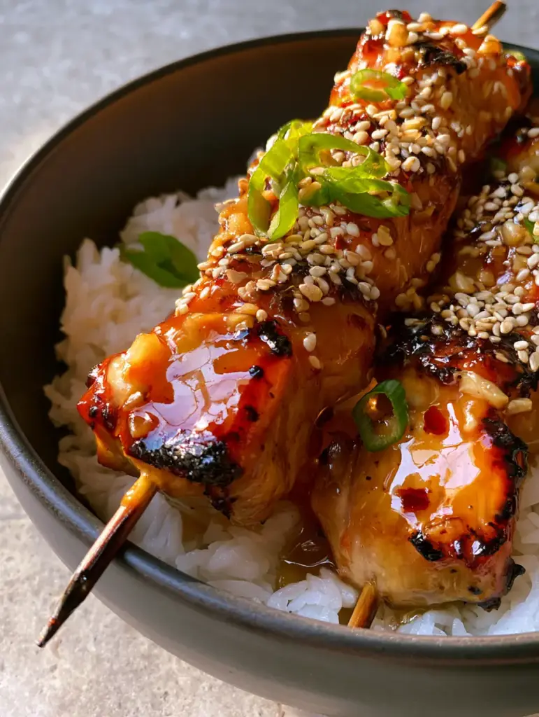 Close-up of charred honey garlic chicken skewers showing the caramelized edges and sesame seed topping.
