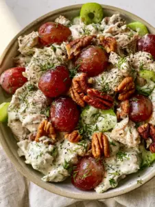 Macro top-down shot of chicken salad with grapes showing hand-pulled shreds and glistening red grapes in ivory dressing.