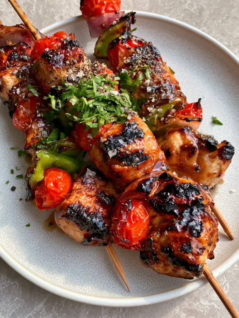 Oversized chunks of grilled chicken breast on skewers with charred red onion and green bell pepper edges.